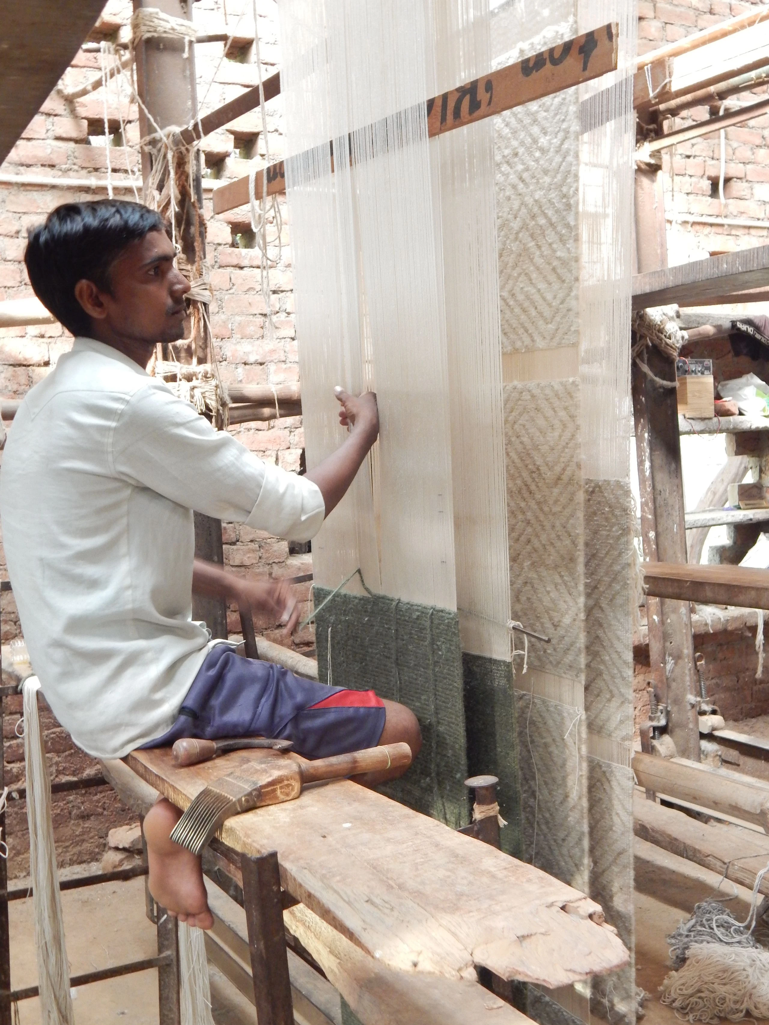 Skilled artisan weaver hand-looming a custom rug on a vertical loom at Kaleen