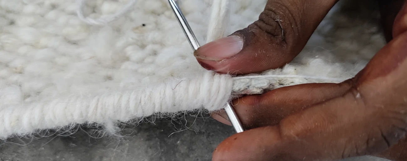 Close up image of an artisan hand serging the border of a custom wool rug from Kaleen, creating a beautiful finished edge