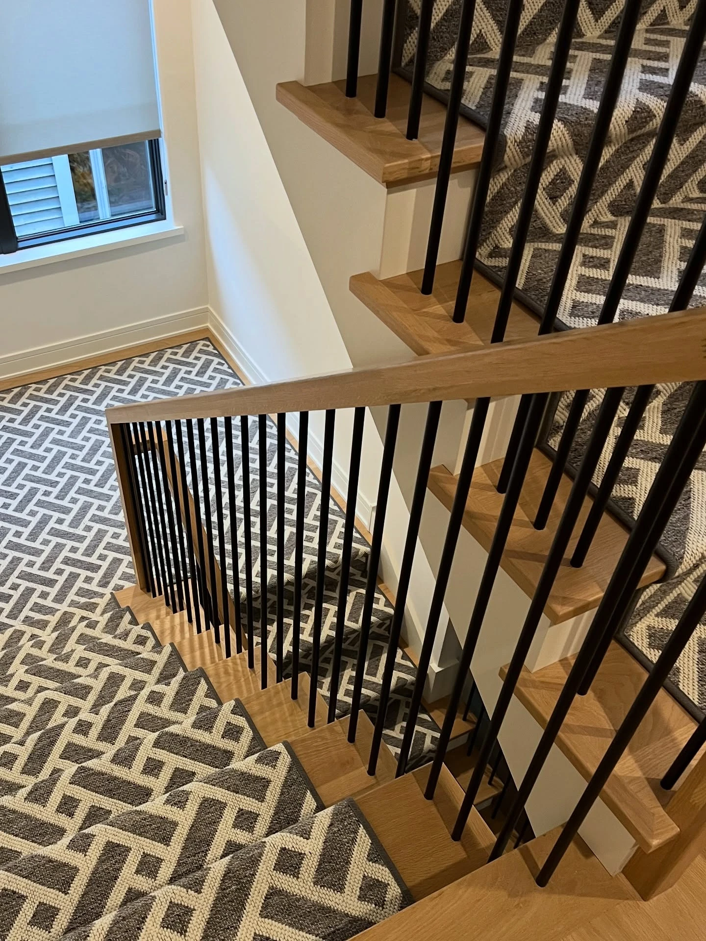  Close up view of a multi level brown wood stair case with a geometric carpet stair runner in grey from Hook and Beam by Kaleen.